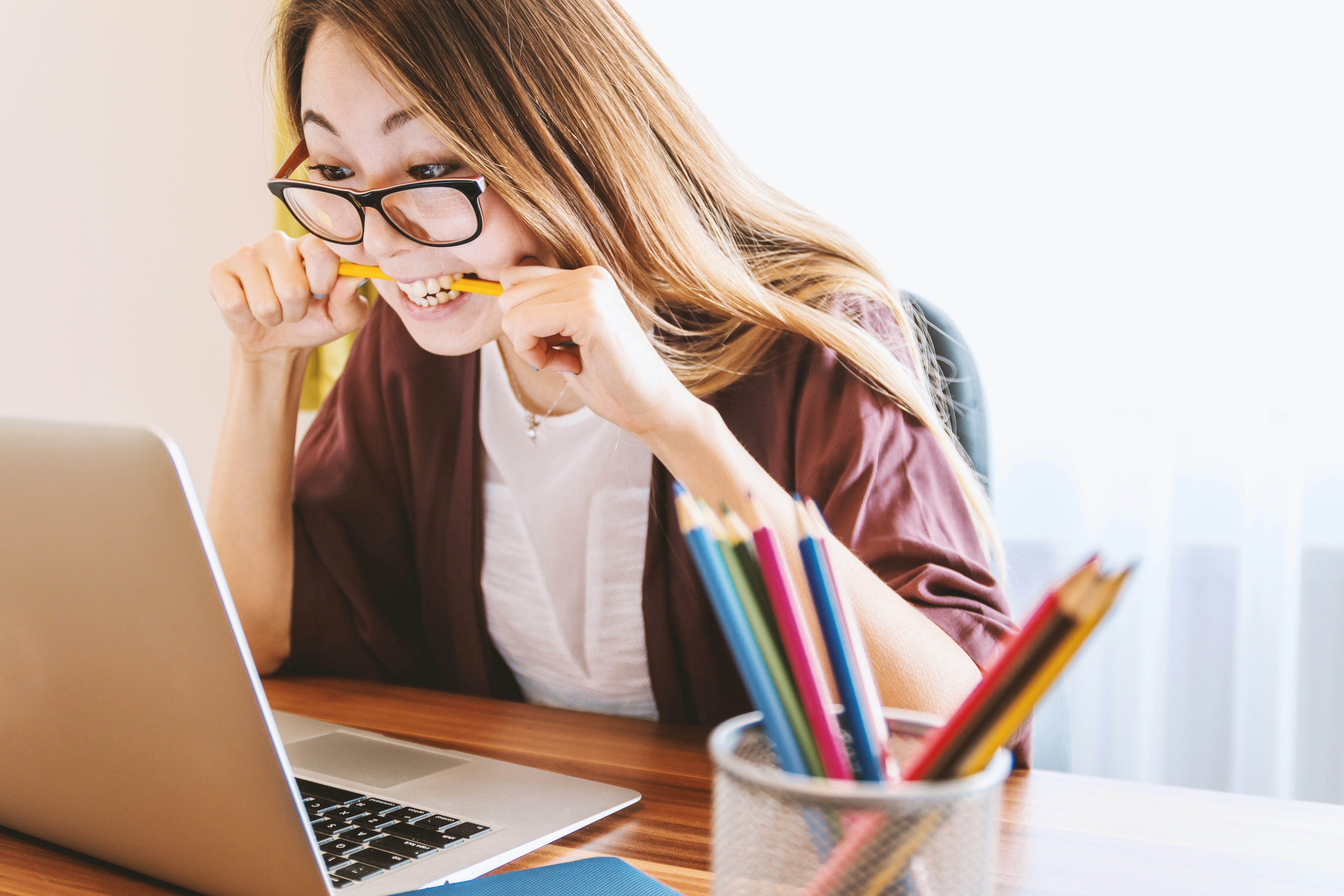 A woman staring at a laptop screen and biting a pencil in desperation due to exam difficulty